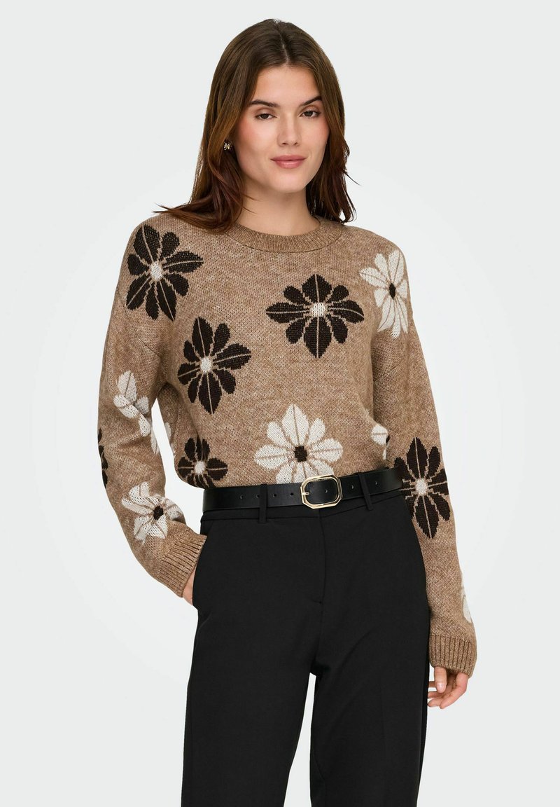 Suéter de punto en marrón claro con patrones florales en negro y blanco. Presenta un cuello redondo y puños acanalados, combinado con pantalones negros de cintura alta.