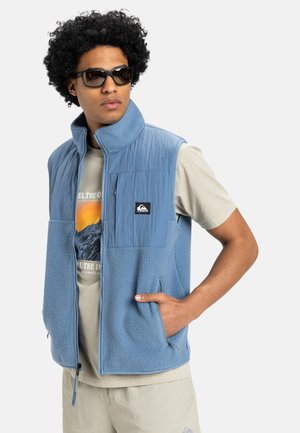 Hellblauer Fleecepullover mit hohem Kragen, strukturiertem blauen Frontpanel, Reißverschlusstaschen und einem Logopatch auf der Brust.
