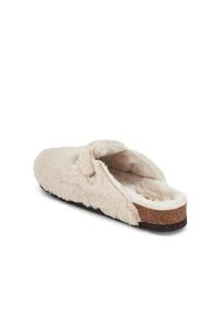 Chausson en mousse, rose pâle, avec une texture douce et pelucheuse et une semelle en liège. Présente un dos ouvert et un accent en nœud sur le dessus.