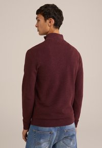 Pulover burgund cu guler înalt, textură tricotată, manșete și tiv cu nervuri, purtat cu blugi din denim albastru deschis.