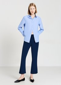Chemise bleu clair à col, portée avec un pantalon évasé bleu marine et des ballerines noires à bout pointu ; tissu lisse et design structuré.