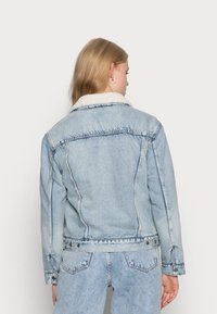 Lichtblauwe denimjack met een sherpa-kraag, voorzien van voor- en achterste schoudernaad, zijzakken en knoopsluitingen.