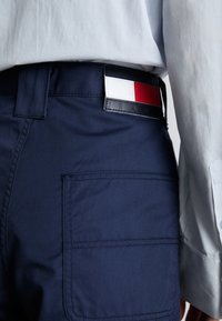 Marineblauwe broek van katoenmix, met een achterzak en een multicolore patch op de tailleband met rode, witte en blauwe accenten.