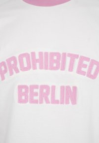 Weißer Stoff mit geschwungenen, rosa, strukturierten Buchstaben, die "PROHIBITED" buchstabieren, und darunter gerade, rosa Buchstaben mit der Aufschrift "BERLIN".
