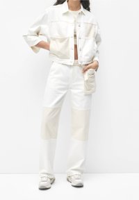 Biała i beżowa dżinsowa kurtka z kieszeniami z klapkami oraz skróconym krojem, połączona z dopasowanymi spodniami na wysokim stanie z kolorowym blokowaniem. Sneakersy w zestawie.