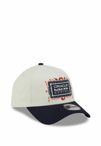 Baseballkappe mit einer weißen Krone und einem marineblauen Schirm. Verfügt über ein bunt gesticktes Logo auf der Vorderseite und eine textile Struktur.