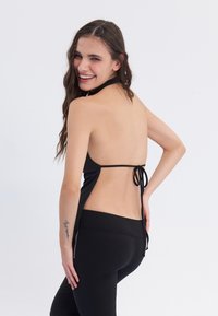Crni top na halter s otvorenim leđima, vezan u struku. Uparen s crnim tajicama visokog struka s detaljom bočnog patentnog zatvarača.