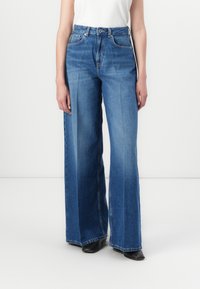 Jeans de denim azul de perna larga com cintura alta, apresentando um fecho de botão, cinco bolsos e costura limpa. Tecido texturizado para durabilidade.