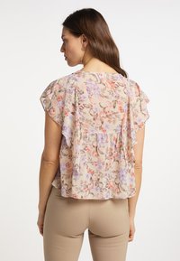 Blusa floreale con uno sfondo beige chiaro, fiori rosa e viola, maniche a farfalla e una vestibilità morbida e rilassata.