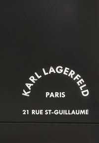 Piele neagră texturată cu text alb embosat: "KARL LAGERFELD PARIS 21 RUE ST-GUILLAUME" într-un design arcuit.