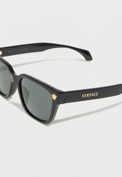 Μαύρα ορθογώνια γυαλιά ηλίου με σκοτεινούς φακούς, χρυσό λογότυπο Versace στο πλαϊνό μπράτσο και έμβλημα Μέδουσας στη μπροστινή γωνία.
