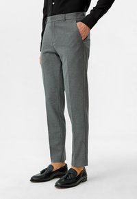 Grijze pantalon met een getailleerde pasvorm, stoftextuur die lijkt op fijne weving, en zijzakken. Draag met zwarte instappers en een zwart shirt.