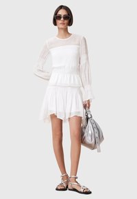 White, long-sleeve dress with a smocked bodice and layered skirt. Paired with silver sandals and a metallic silver bag.