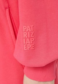 Felpa fucsia con maniche che presentano un logo in rilievo "PATRIZIA PEPE" in un colore abbinato, evidenziando un tessuto liscio e un polsino a costine.