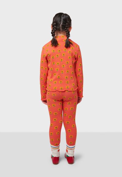 Two-piece children's outfit featuring an orange top and leggings with yellow sunflower patterns. Ribbed texture and layered hem details.