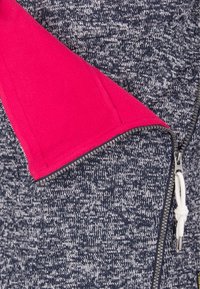 Grå och vit texturerad tyg med en klar rosa accent. Har en dragkedja och en snörning som stängning. Inkluderar en fickdetalj.