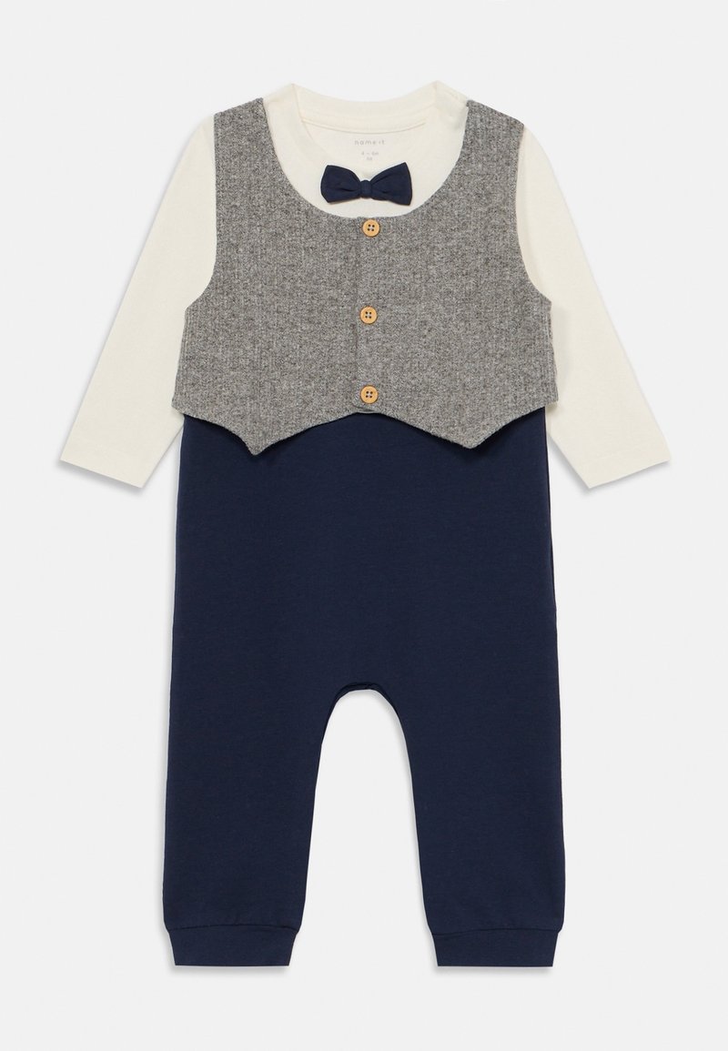 Combinaison marine avec une chemise à manches longues crème clair, un gilet gris par-dessus, des boutons en bois et un nœud papillon marine. Tissu doux et coupe décontractée.