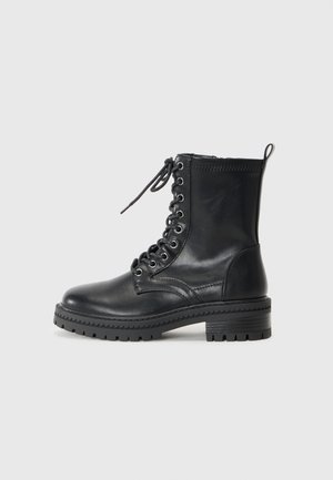 Bottine noire en cuir avec un bout rond, des lacets à l'avant et une semelle en caoutchouc épaisse. Présente des détails de couture et une languette à l'arrière.