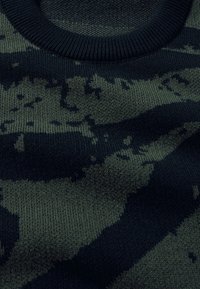 Gros plan d’un tissu tricoté avec un motif camouflage vert foncé et noir et un col rond en côtes.