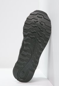 Musta kuminen kenkäpohja, jossa on teksturoitu kuvio syvennyksillä ja hankauspintojen eroilla pitoa varten. "new balance" -logo on painettu sivuun.