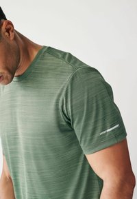Grøn atletisk t-shirt med korte ærmer, tekstureret stof, rund hals og en hvid accentstribe på venstre ærme.