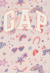 Medvilninė marškinėliai su ryškiu balintu tekstu "GAP", papuošti spalvingais piešiniais, įskaitant gėles, širdis ir raštus ant šviesiai rožinės fono.