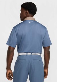 Nike golfa polo krekls gaiši zilā krāsā ar beigu krāsu apkakli, īsām piedurknēm un mazu baltu logo aizmugurē. Gluda auduma struktūra.