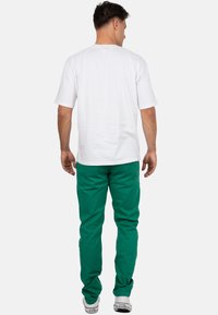 T-shirt bianco a maniche corte abbinato a pantaloni verdi; i pantaloni hanno una vestibilità comoda; il modello indossa sneakers bianche. Design semplice e informale.