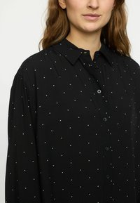 Schwarze Button-up-Hemd aus weichem Stoff, mit weißen Punkte-Mustern, einem klassischen Kragen und langen Ärmeln mit lockerer Passform.