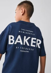 Mørkeblå bomulds polo skjorte med hvidt oversized tekst: "BAKER" og "by TED BAKER" på ryggen, med yderligere trykdetaljer ovenfor.