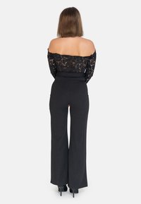 Top in pizzo nero senza spalle abbinato a pantaloni a vita alta neri a gamba larga; tessuto liscio con una leggera lucentezza, dettagli con tacco.