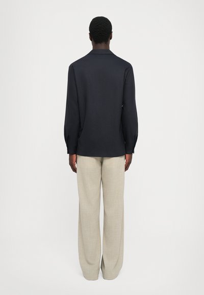 Sötétkék hosszú ujjas ing, gallérral, hátán redős részlettel, beige széles szárú nadrág, textúrált anyagból. Egyszerű stílus, testre szabott fazon.