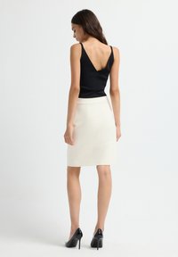 Zwarte mouwloze top met een V-rug, gecombineerd met een witte kokerrok. Het model draagt zwarte hoge hakken en toont een soepele, slanke silhoutte.