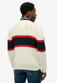 Pull en tricot avec un motif en torsades, couleur crème, et des rayures horizontales contrastées en bleu marine et rouge. Détails en côtes aux poignets et à l'ourlet.