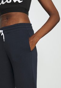 Mörkblå mjukisbyxor med dragsko i midjan, sidofickor och mjukt bomullsmaterial, tillsammans med en svart kort topp med vita bokstäver.