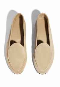 Zapatos de ante beige tipo slip-on con punta redondeada, costuras cosidas y un forro interior suave. Suela plana con un diseño minimalista.