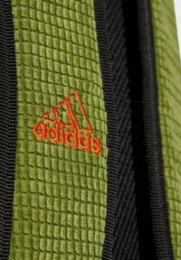 Zelená textúrovaná tkanina s mriežkovým vzorom, čiernymi akcentmi a vyšitým oranžovým logom Adidas.