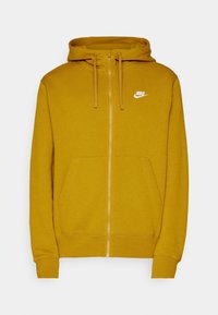 Sudadera con cremallera Nike en color mostaza, que cuenta con una capucha con cordón, bolsillos frontales, puños acanalados y un logo blanco en el pecho.