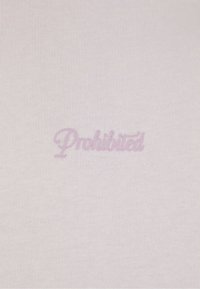 Un tessuto rosa chiaro presenta una superficie texturizzata con la parola "Proibito" ricamata in modo sottile in un font corsivo dello stesso colore.
