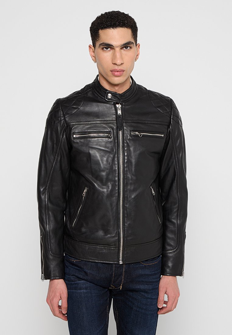 Chaqueta de cuero negra con cuello alto, cierre frontal con cremallera y múltiples bolsillos con cremallera. Presenta hombros acolchados y un diseño ajustado.