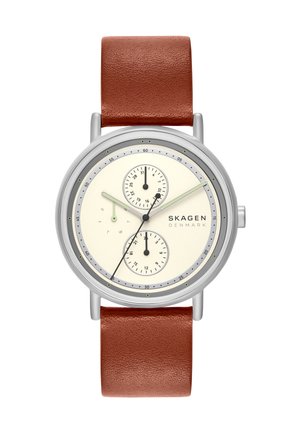 Montre ronde argentée avec cadran crème, bracelet en cuir marron, trois sous-cadrans pour la date, le jour et l'heure 24h, avec la marque Skagen Denmark.