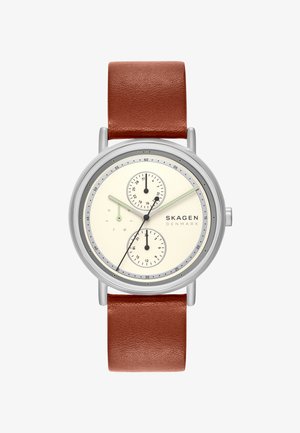 Orologio tondo color argento con quadrante crema, cinturino in pelle marrone, tre sottoquadranti per data, giorno e ora 24, e marchio Skagen Denmark.