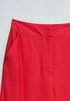 Jupe rouge taille haute avec une texture lisse et une fermeture avant cachée, présentée sur un fond clair uni.