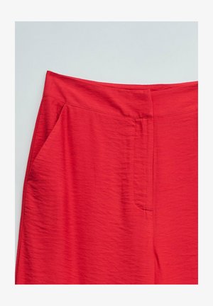 Jupe rouge taille haute avec une texture lisse et une fermeture avant cachée, présentée sur un fond clair uni.