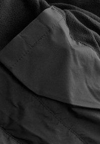 Schwarzer Fleece-Bekleidungsstück mit glatter, matter Textur; verfügt über Nähdetails und überlappende Stofflagen für Wärme und Komfort.