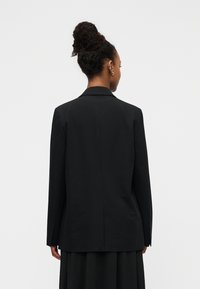 Μαύρο σακάκι με δομημένο σχέδιο, εφαρμοστή γραμμή, μακριά μανίκια και γιακά με εγκοπές. Διαθέτει ομαλή ύφανση και ελάχιστες ραφές.