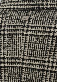 Tessuto misto lana in un motivo a quadri bianco e nero. Presenta una texture morbida con un accento di logo metallico e quadrati intrecciati distintivi.