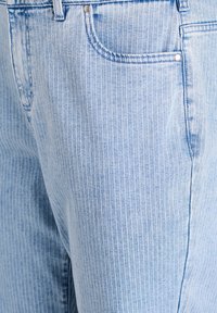 Svetlomodré riflové džínsy s pruhmi, ktoré majú viditeľné predné vrecko, detail z kovových nitov a jemnú textúru s jemným pružením.