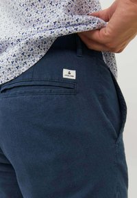 Pantaloni scurți bleu marin, confecționați dintr-un material ușor, având o cataramă la spate și un mic etichetă albă pe care este brodat textul "JACK & JONES".