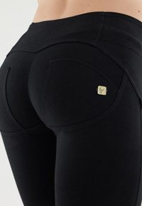 Leggings neri con un distintivo design della tasca curvata e un piccolo logo sul lato destro, realizzati in tessuto elasticizzato.